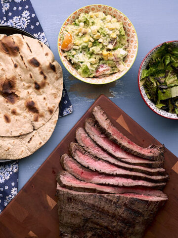 Grilled sliced carne asada tacos with grilled tortillas, elote guacamole, and charred romaine slaw