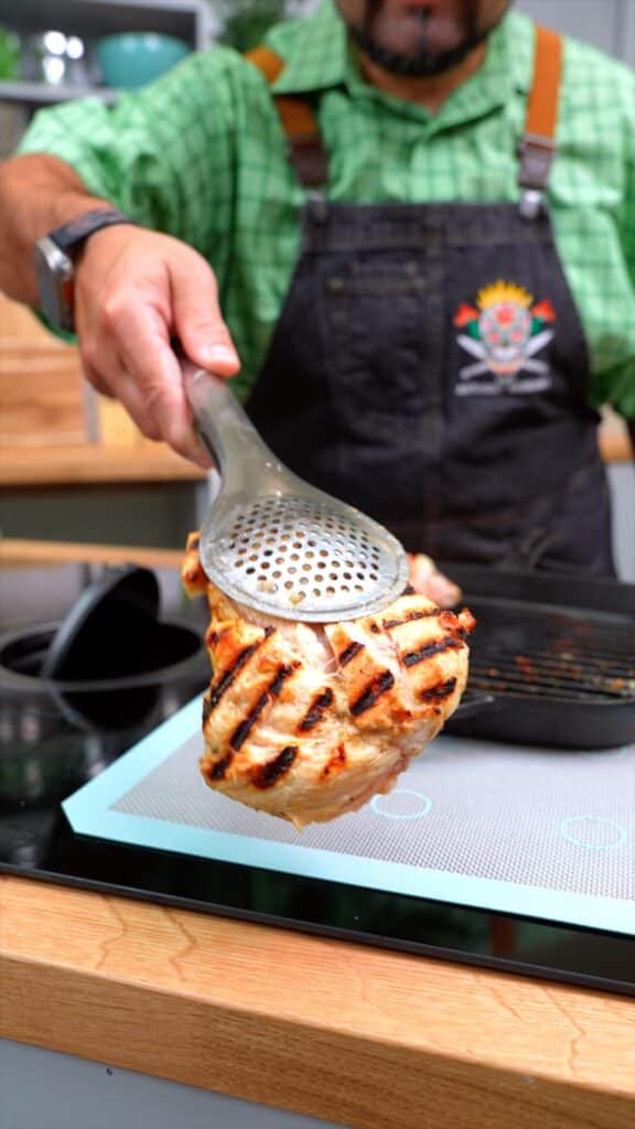grilled chicken held by tongs in front of Chef Anthony Serrano